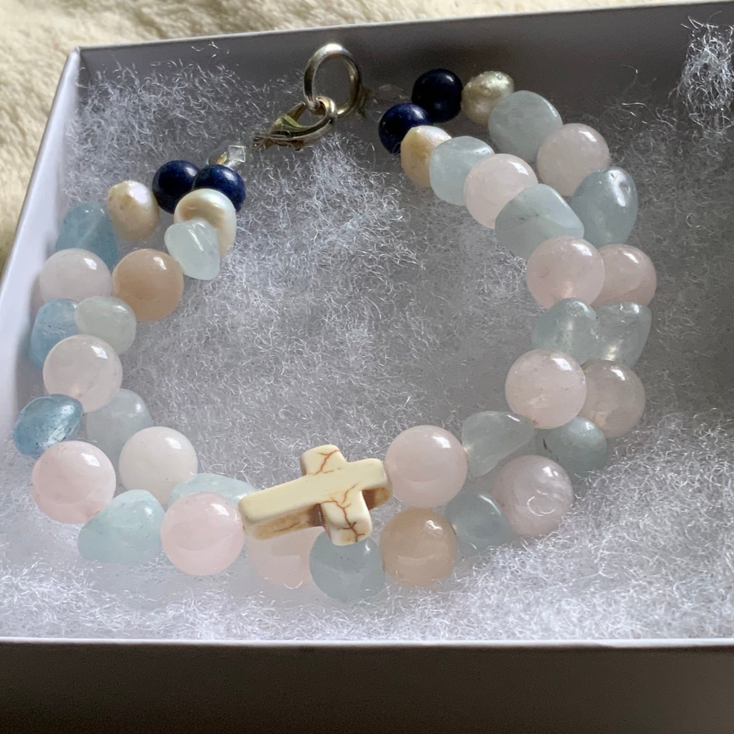 Beaded bracelet with a cross charm in a box on a soft surface