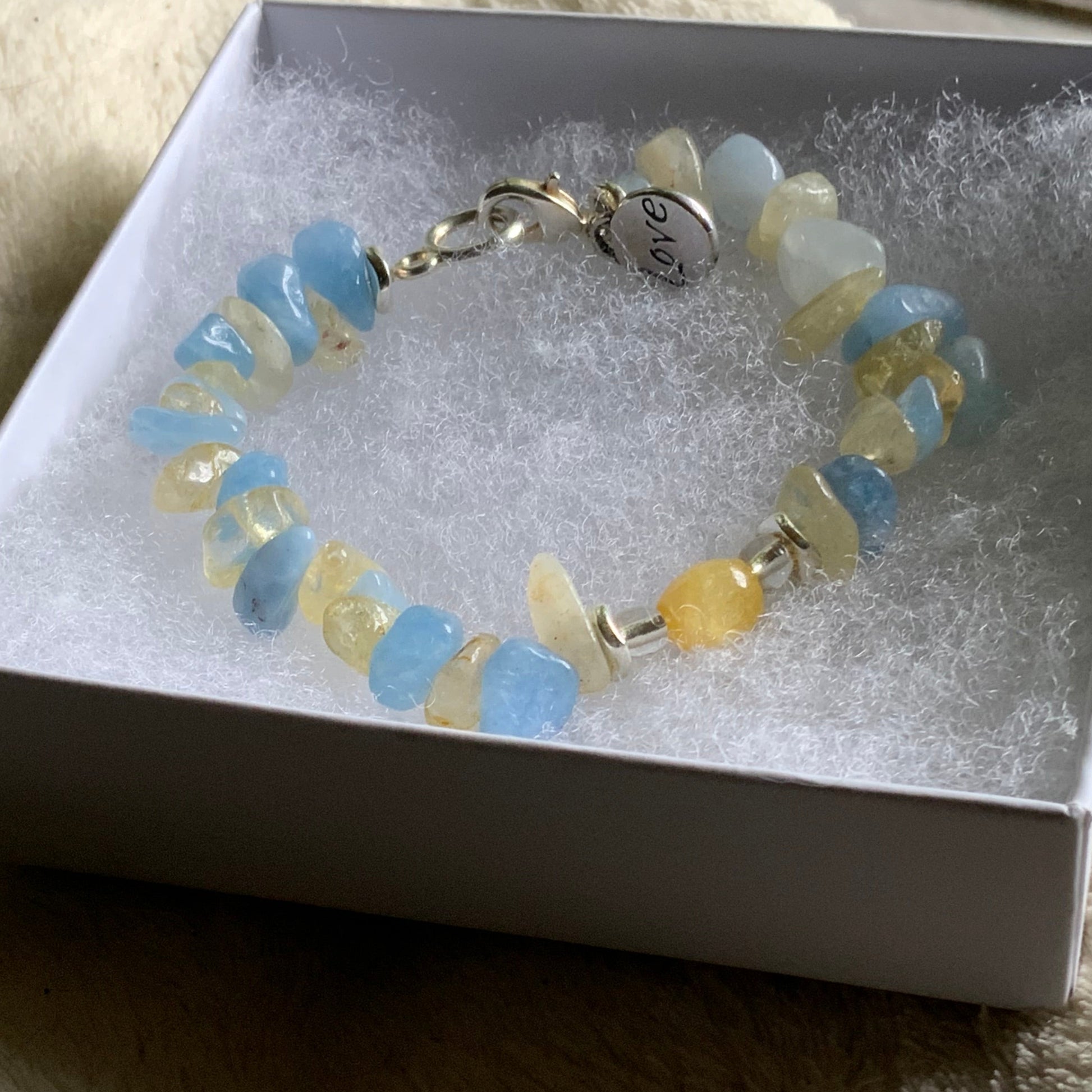 Bracelet with blue and yellow beads on a gray box, placed on a textured surface.