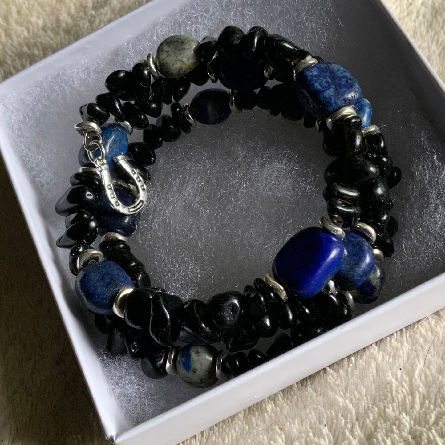 Black and blue beaded bracelet with a silver charm on a white box.
