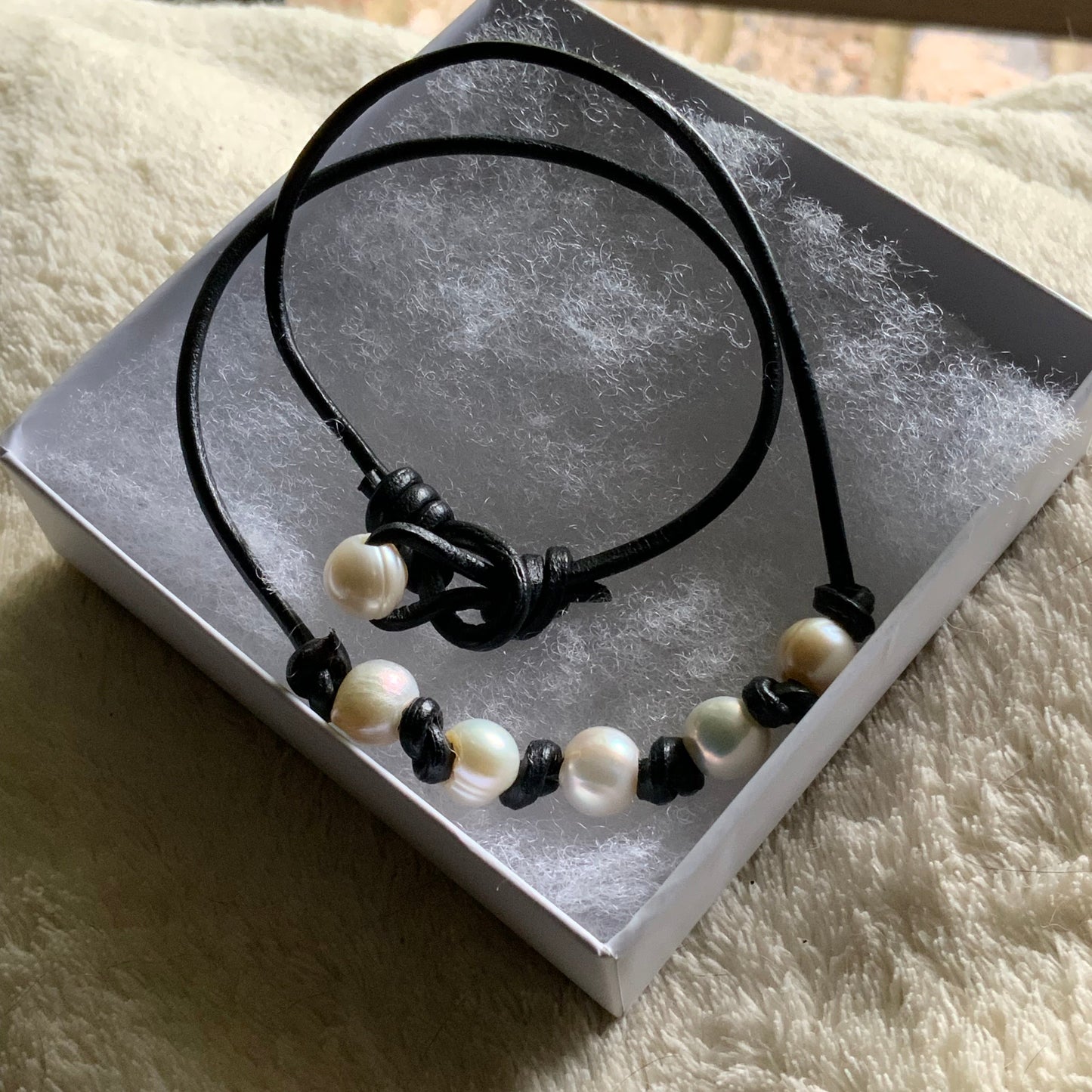 Black and white pearl necklace on a gray card with a textured beige surface background