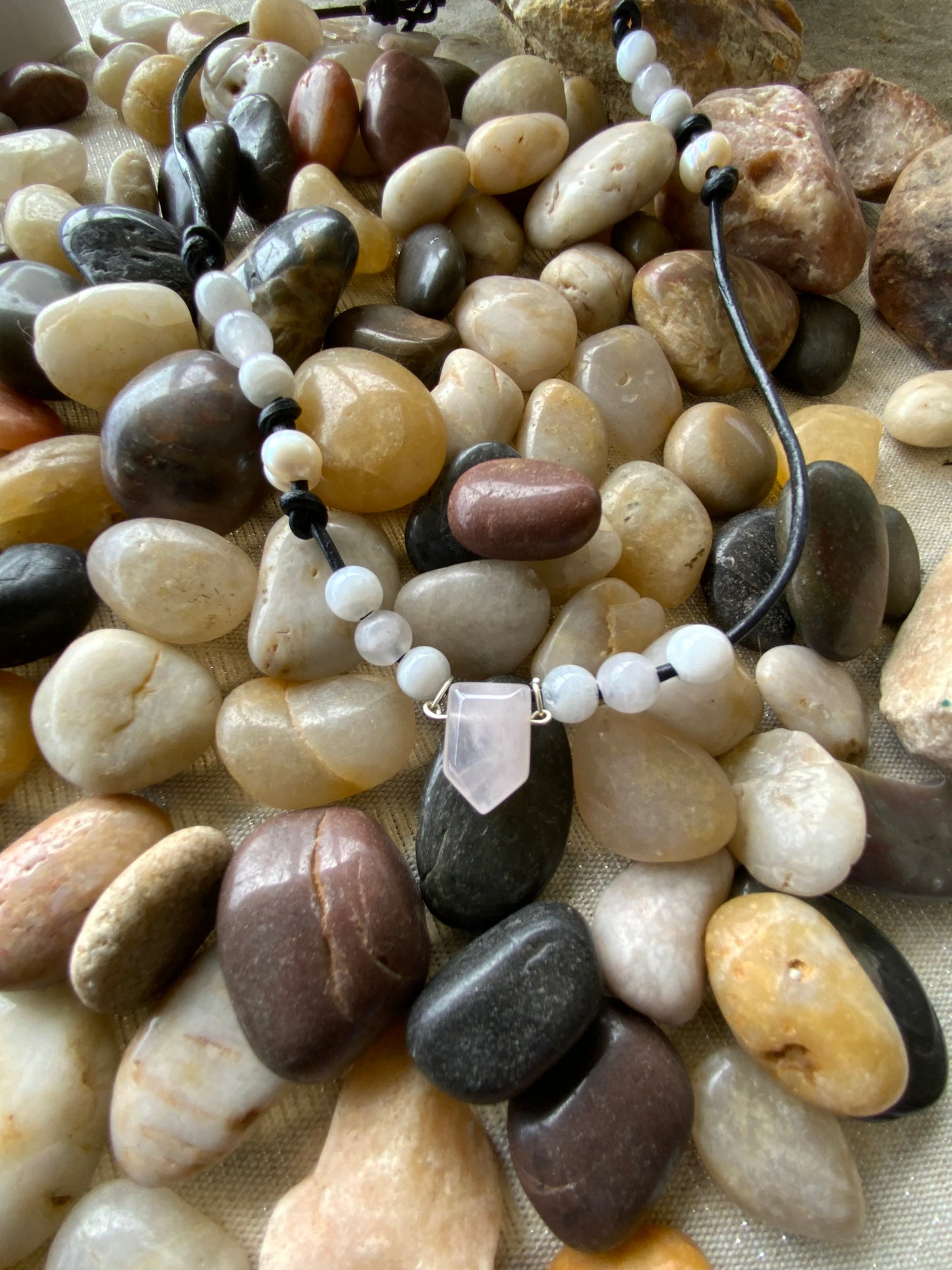 Necklace with white beads and black cord on a bed of multicolored pebbles