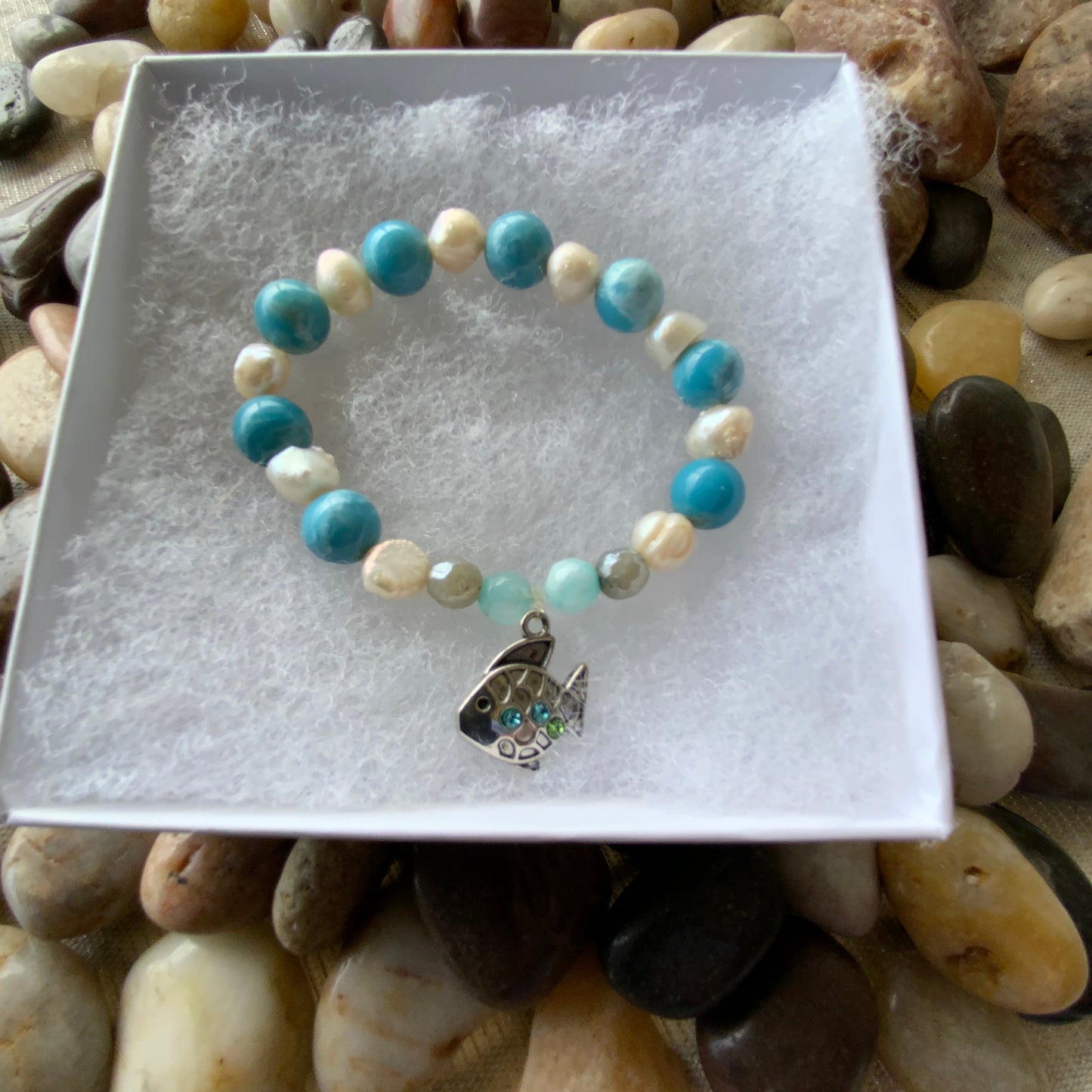 Bracelet with pearls and reconstituted larimar beads on a white card, surrounded by pebbles.