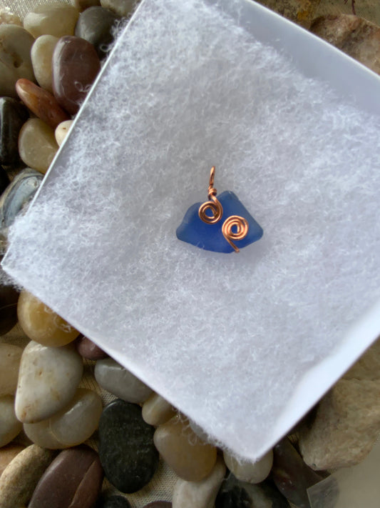 Blue sea glass with a copper coil on a white cloth, surrounded by pebbles.